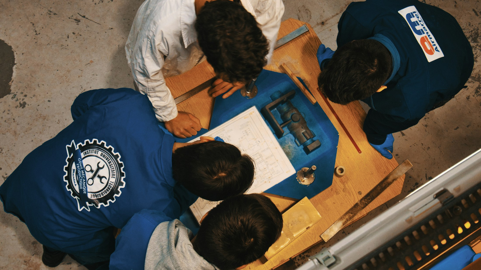 An engineering team reviewing drawings and components around a workbench.