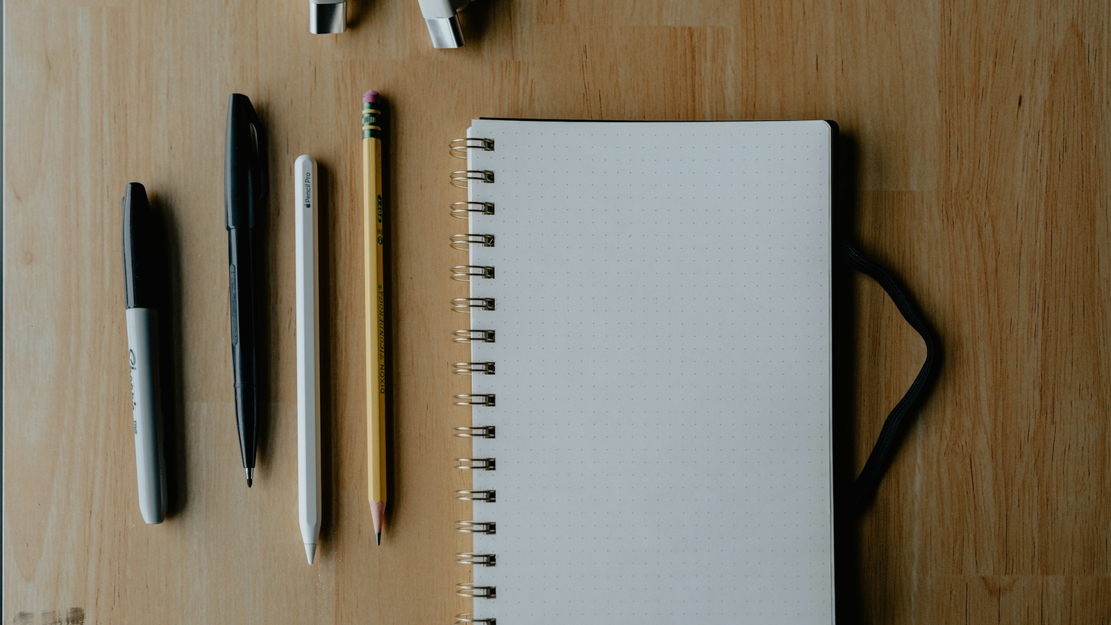 A closed notebook with neatly arranged pens, pencils and earphones on a wooden table.